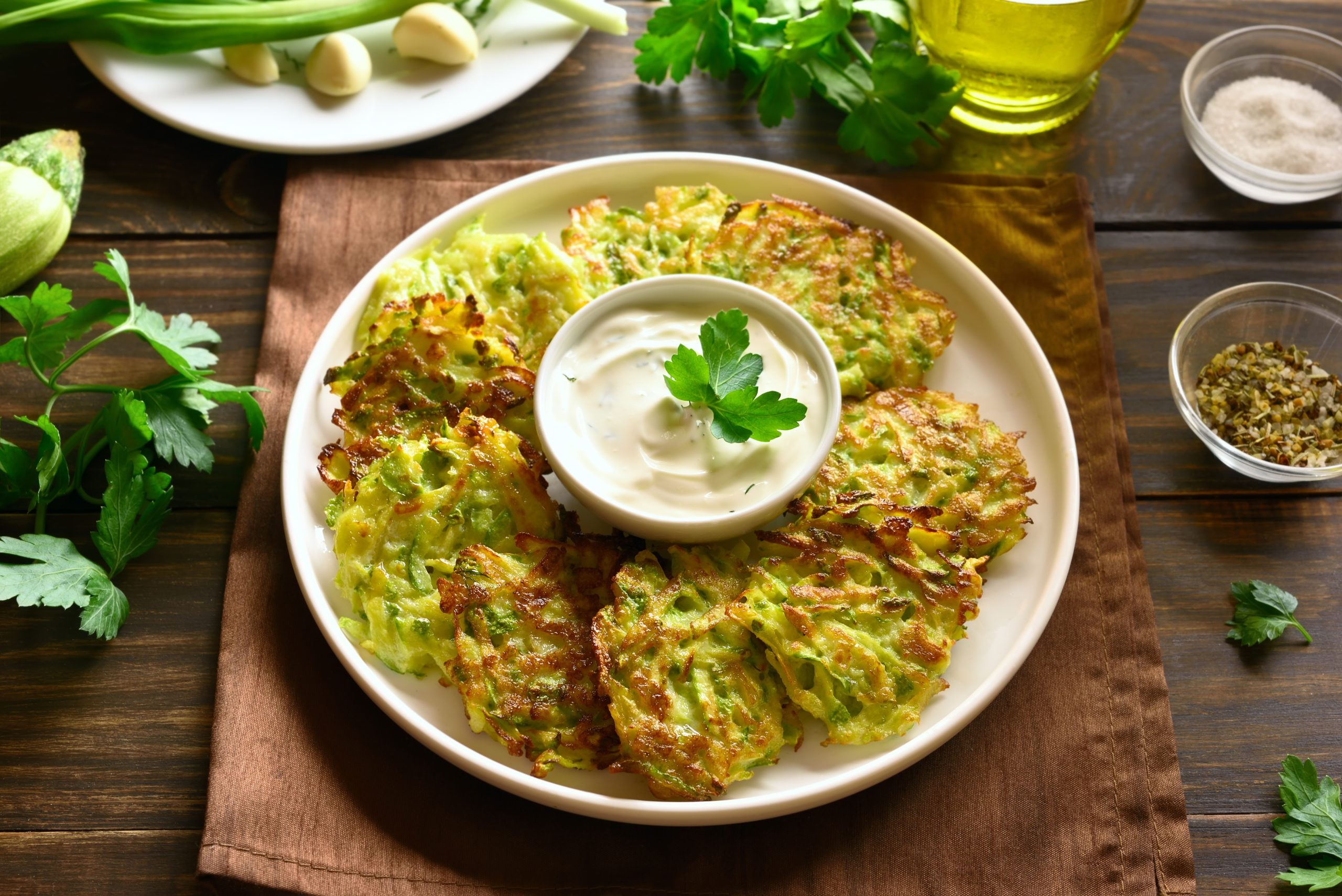 pancakes made with zucchini on a white plate served with a sour cream sauce in a white bowl